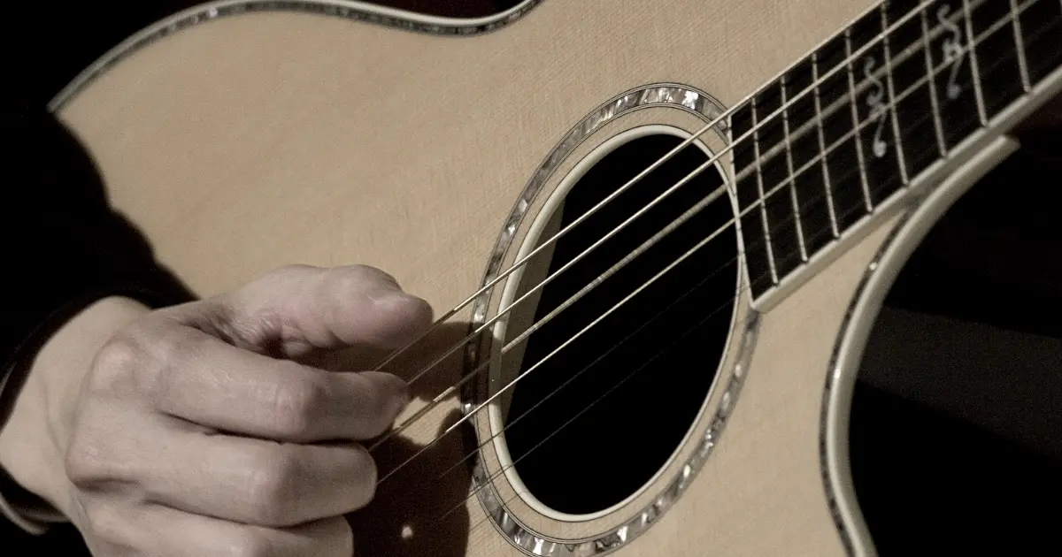 Close-up of JOHN ISHIHARA playing acoustic guitar.