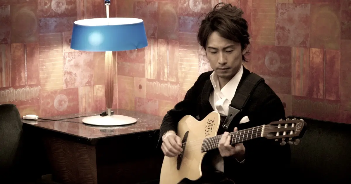 Professional monochrome portrait of JOHN ISHIHARA playing guitar, featuring his upper body in a high-contrast style.